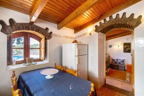 A room with a wooden ceiling, a dining table with a blue tablecloth, a white refrigerator, and a window with a view of greenery. - Villa 'Casa da Maria Teresa V5' with Private Pool, Wi-Fi, and Air Conditioning (Santa Catarina da Fonte do Bispo)