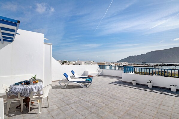 Eine Dachterrasse mit Tisch, Stühlen, Liegestühlen und Pflanzen in Töpfen.