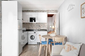 A compact kitchen with a washing machine, a microwave, and a sink. There is a dining area with a table and chairs.