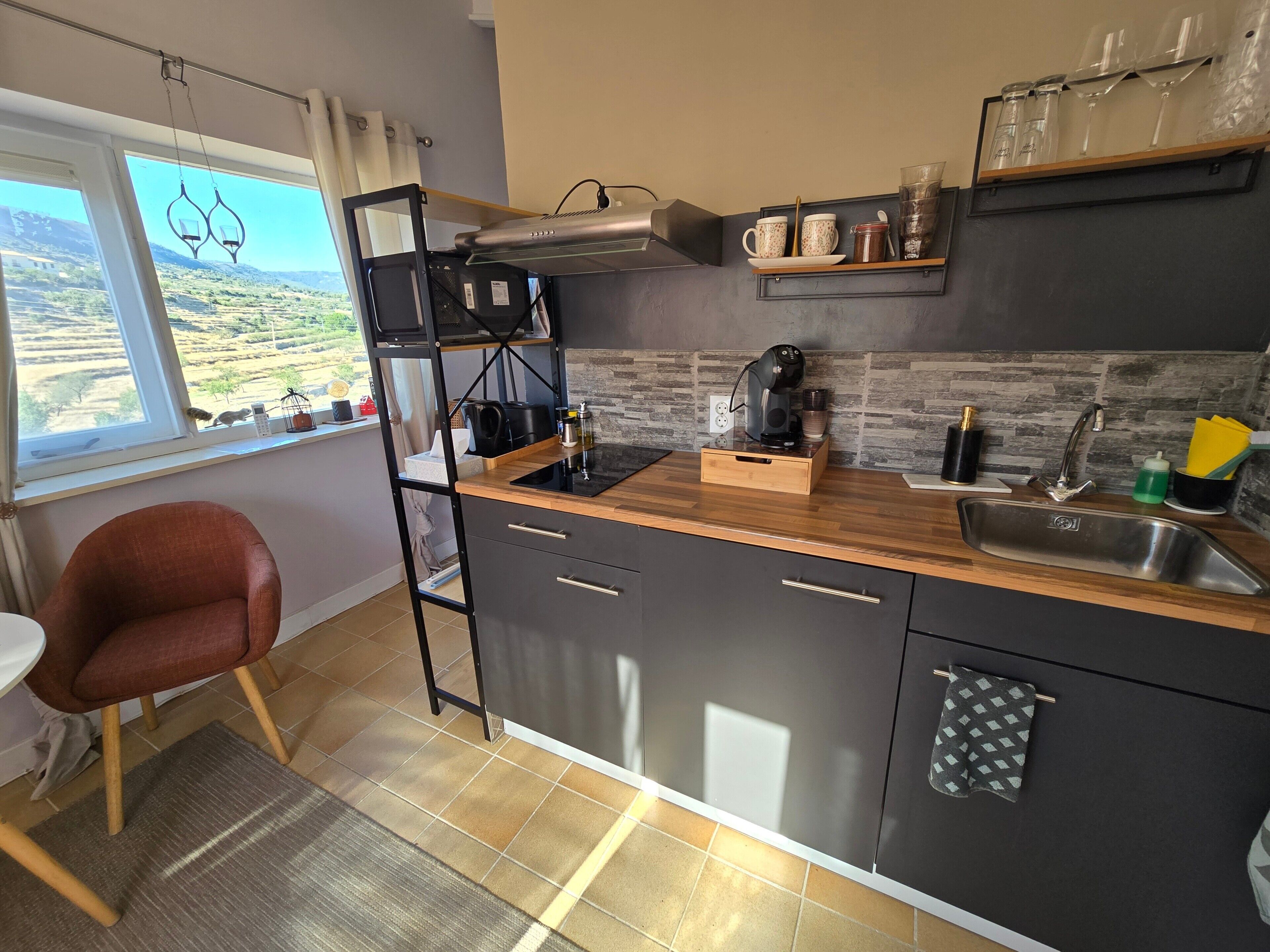 A compact kitchen with a wooden countertop, a built-in stove, a sink, and a window with a view of the countryside.