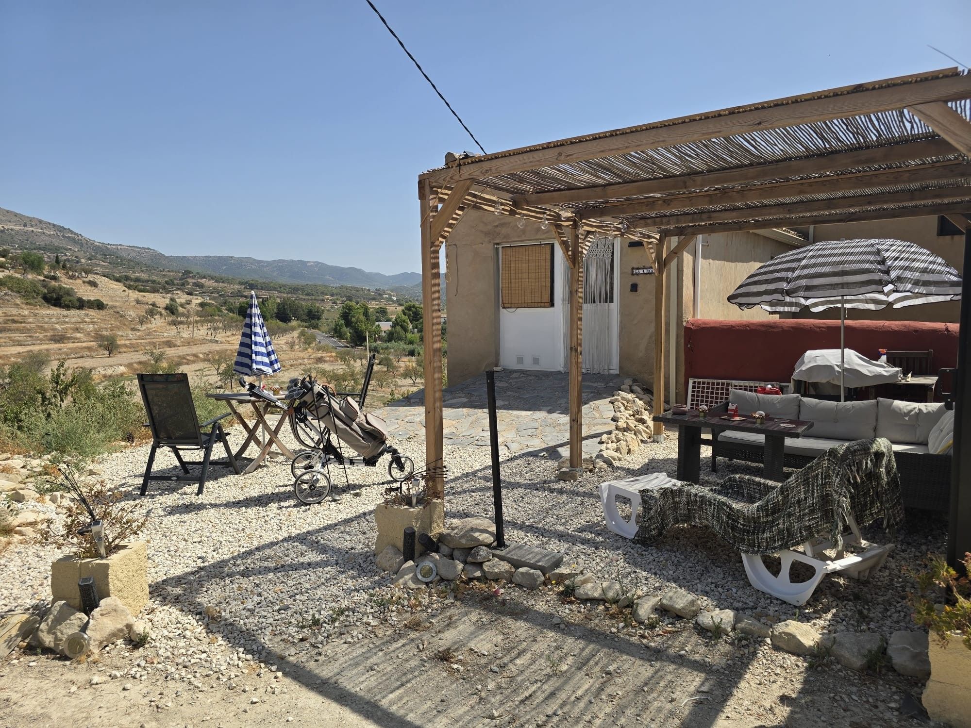 A covered outdoor seating area with a table and chairs, a bicycle, and a view of the surrounding landscape.