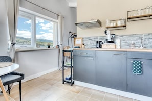 A modern kitchen with grey cabinets, a window with curtains, a dining area with a table and chairs, and a view of the outdoors.