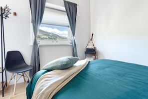 A bedroom with a bed, a chair, a window with curtains, and a view of the outdoors.