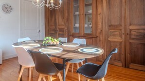 Un coin repas avec une table ronde, des chaises, un lustre, des meubles en bois et une horloge au mur.