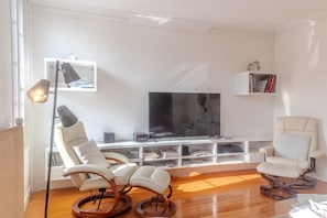 Una sala de estar con televisor, dos sillones, una estantería y una lámpara.