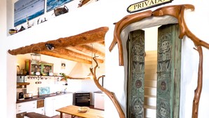 Une cuisine avec un plafond orné de poutres en bois, une table à manger et un banc. Une pancarte au-dessus de la porte indique : « ENTRÉE INTERDITE ».