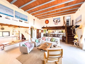 A spacious living area with a high ceiling, rustic wooden beams, a dining area, and a staircase. - Holiday Home 'Can Picca' with Sea Views, Private Pool and Wi-Fi (Illes Balears)