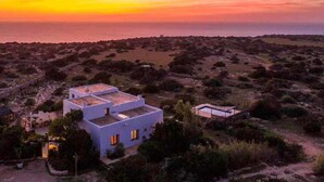 Une maison moderne dotée d’un toit plat, entourée d’un paysage aride où la végétation est rare.