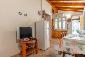Una cocina compacta con refrigerador, televisor sobre un soporte de madera y una mesa de comedor con mantel.
