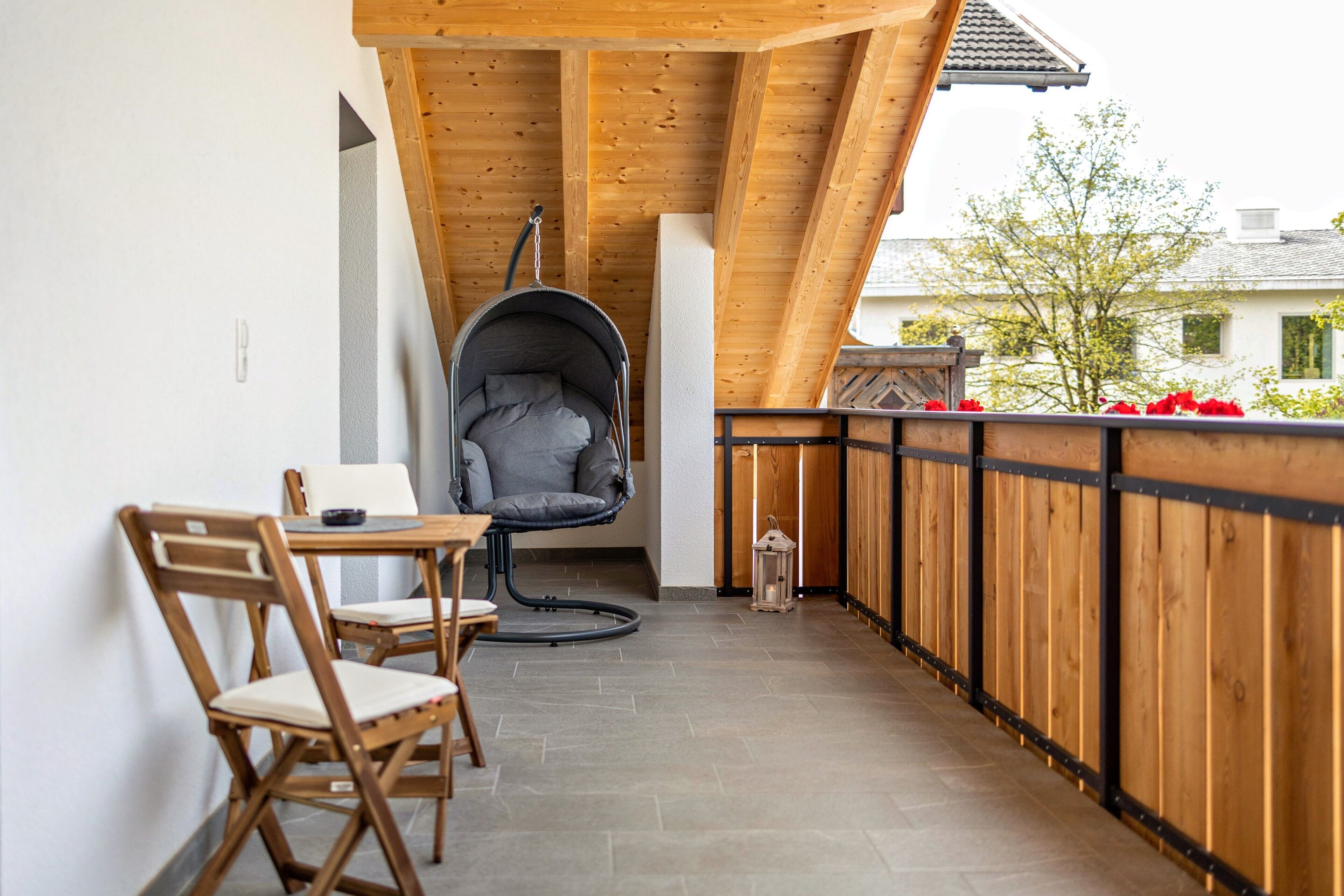 A wooden balcony with a hanging chair, a table, and chairs.