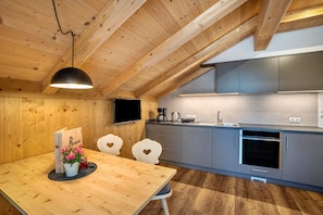 A modern kitchen with wooden ceiling beams, a dining area with a table and chairs, and a built-in TV. - Apartment 'Krämerhof Apt Villnösser Geisler' with Mountain View, Shared Garden and Wi-Fi (Rodengo)