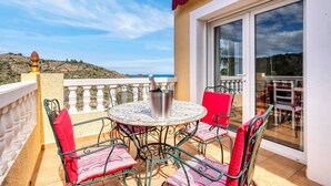Ein Balkon mit Tisch und Stühlen, Blick auf das Meer und ein Berg im Hintergrund.