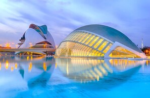 A modern architectural building with a unique curved design, a large reflective pool in front, and a clear sky.