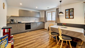 Una cocina moderna con armarios grises, una mesa de comedor con dos sillas y una ventana con cortinas.