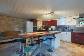 A kitchen with a wooden table, bar stools, a stone wall, and a stone floor.