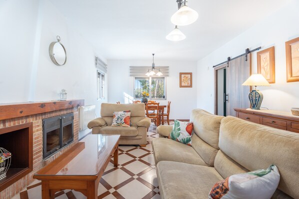 Sala de estar com lareira, sofá, mesa de centro e área de jantar com cadeiras e mesa.