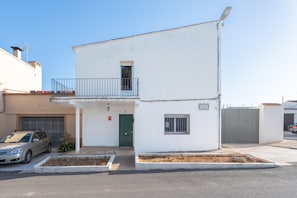 Um edifício de dois andares com uma porta verde, uma pequena varanda e um carro estacionado na entrada.