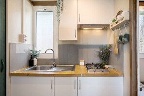 Una cocina con encimera de madera, pileta de acero inoxidable, alacenas blancas, estufa a gas y ollas colgantes.