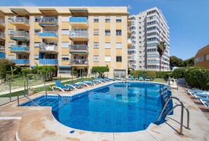 Une piscine avec des chaises longues, un bâtiment doté de balcons et un ciel dégagé.