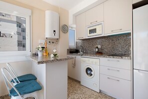 Une cuisine compacte équipée d’un lave-linge, d’un four à micro-ondes et d’un chauffe-eau.