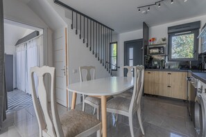 A modern kitchen with a dining area, a staircase, and a view of greenery outside.