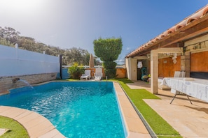 A swimming pool with a tiled deck, a covered patio area, and a small garden.