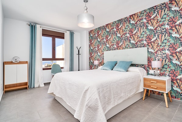 Une chambre à coucher avec un lit, une table de chevet, une lampe et une fenêtre avec des rideaux.