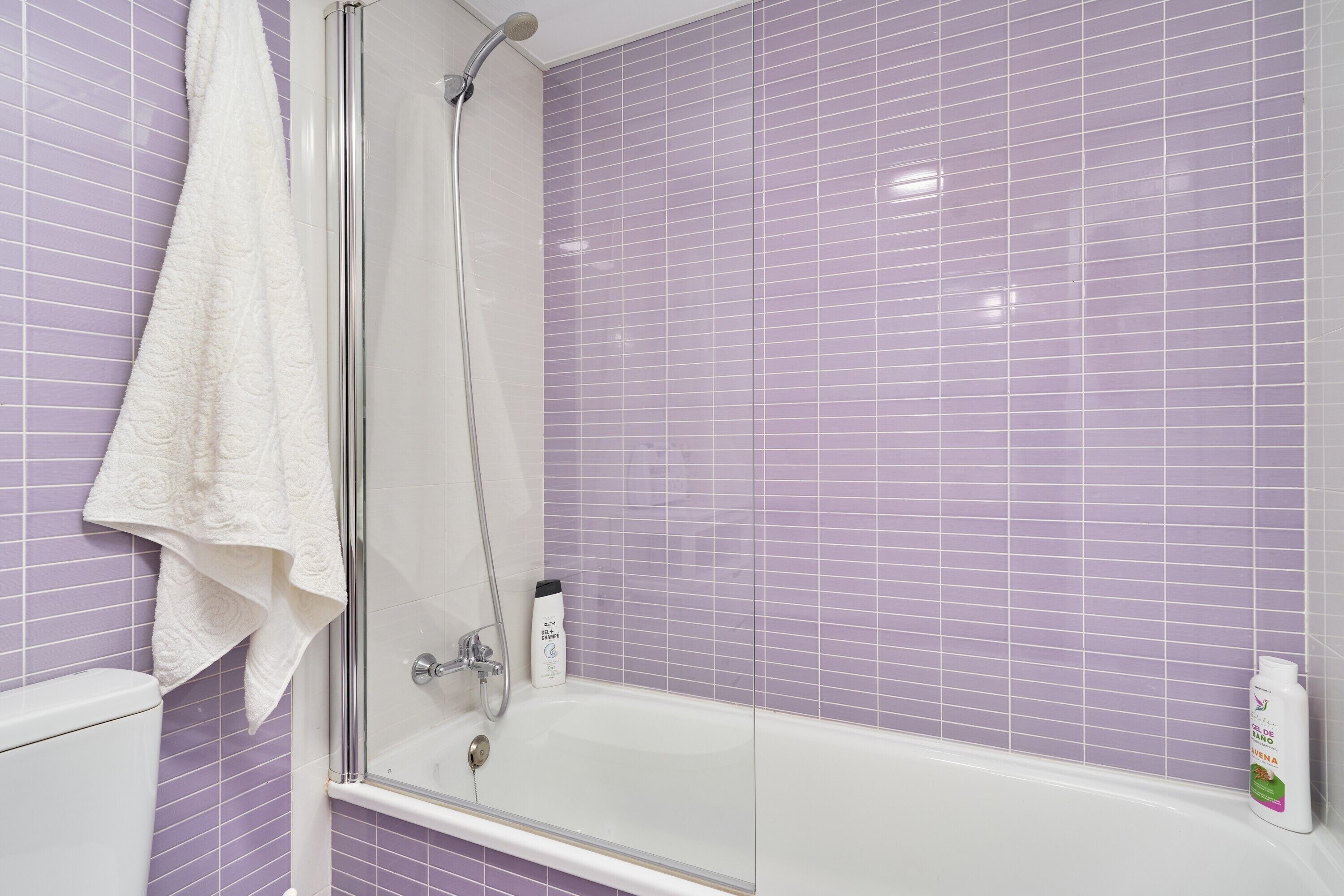Un baño con ducha de vidrio, una bañera blanca y paredes con azulejos morados.