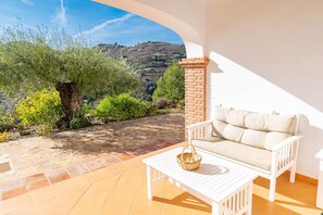 A patio with a white sofa, a wicker basket, and a view of a hilly landscape. - Villa 'Cortijo De La Abuela' with Mountain View, Wi-Fi and Air Conditioning (Málaga)