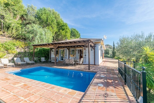 A swimming pool with a pergola and outdoor seating, surrounded by greenery and a tiled patio. - Villa 'Cortijo De La Abuela' with Mountain View, Wi-Fi and Air Conditioning (Málaga)