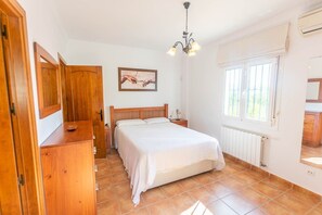 A bedroom with a wooden bed, a nightstand, a desk, a chair, a window, and a radiator. - Villa 'Cortijo De La Abuela' with Mountain View, Wi-Fi and Air Conditioning (Málaga)