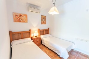 Un dormitorio con dos camas, una mesita de noche con lámpara, un equipo de aire acondicionado y dos cuadros colgados en la pared.