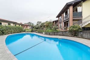 Une piscine entourée d’un jardin aménagé, avec un bâtiment doté de balcons et d’une façade en briques en arrière-plan.