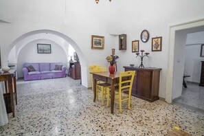 A dining area with a table and chairs, a purple sofa, and a wall with framed pictures and a clock.