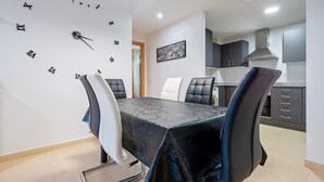 Un coin repas avec une horloge au mur, une table recouverte d’une nappe et des chaises.