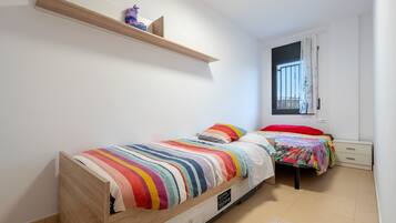 Een slaapkamer met twee bedden, een houten plank, een raam met tralies en een witte muur.
