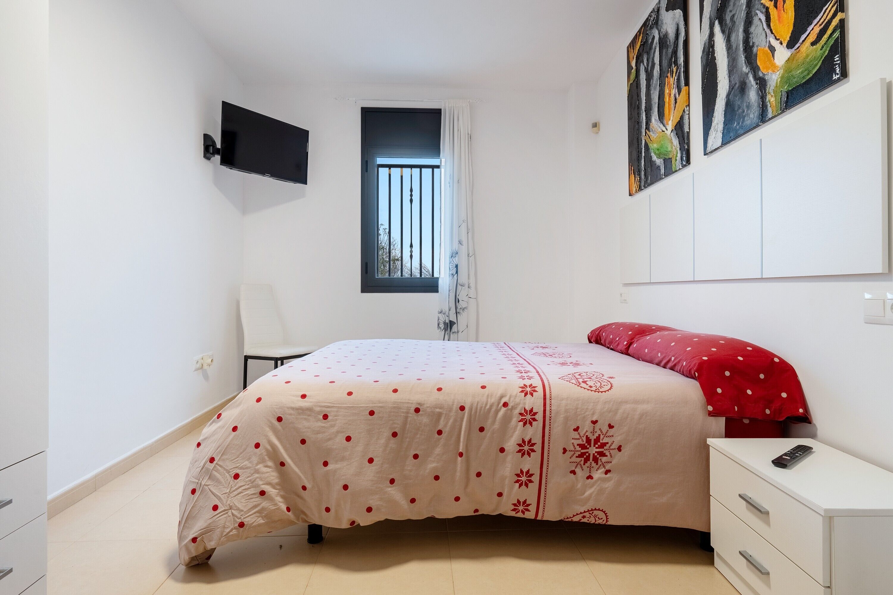 Un dormitorio con cama, una silla, televisor y cuadros en la pared.