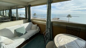 Habitación de hotel con cama, una silla, una mesa y un ventanal con vista a la playa y al océano.