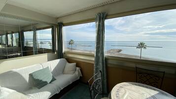Hotelkamer met een bed, een stoel, een tafel en een groot raam met uitzicht op het strand en de zee.