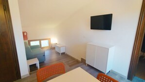 A room with a bed, a TV mounted on the wall, a small table, and a chair.