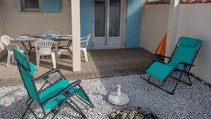 En terrasse med et bord, stole og en lille bålplads, samt en blå dør.