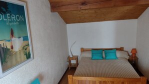Et soveværelse med en træseng, sengetøj med striber, et natbord med lampe, et plakat på væggen og en træbænk.