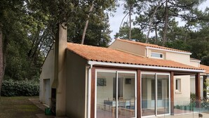 A house with a tiled roof, a glass-enclosed patio, and a garden. - Holiday Home with Shared Pool, Private Terrace and Shared Garden (Saint-Trojan-les-Bains)