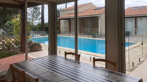 A covered patio area with a pool, a table with chairs, and a view of a residential building. - Holiday Home with Shared Pool, Private Terrace and Shared Garden (Saint-Trojan-les-Bains)