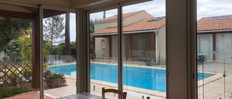 A covered patio area with a pool, a table with chairs, and a view of a residential building.