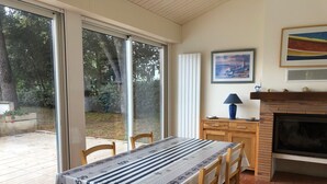 A dining area with a table set for two, a fireplace, and a view through large windows. - Holiday Home with Shared Pool, Private Terrace and Shared Garden (Saint-Trojan-les-Bains)