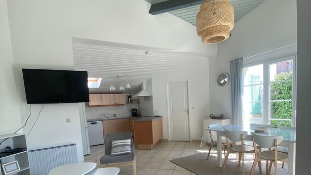 A modern living room with a sofa, a dining area with chairs, a kitchen in the background, and a TV mounted on the wall. - Holiday Home 'Vacances Au Château D'Oléron' with Private Terrace and Wi-Fi (Le chateau d'oleron)