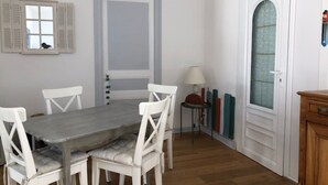 Un coin repas avec une table en bois et des chaises blanches, une porte dotée d’un panneau en verre dépoli et une petite lampe posée sur une table d’appoint.