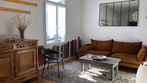 Un salon comprenant un meuble en bois, un fauteuil noir, un canapé marron, une table basse et une grande fenêtre avec des rideaux.