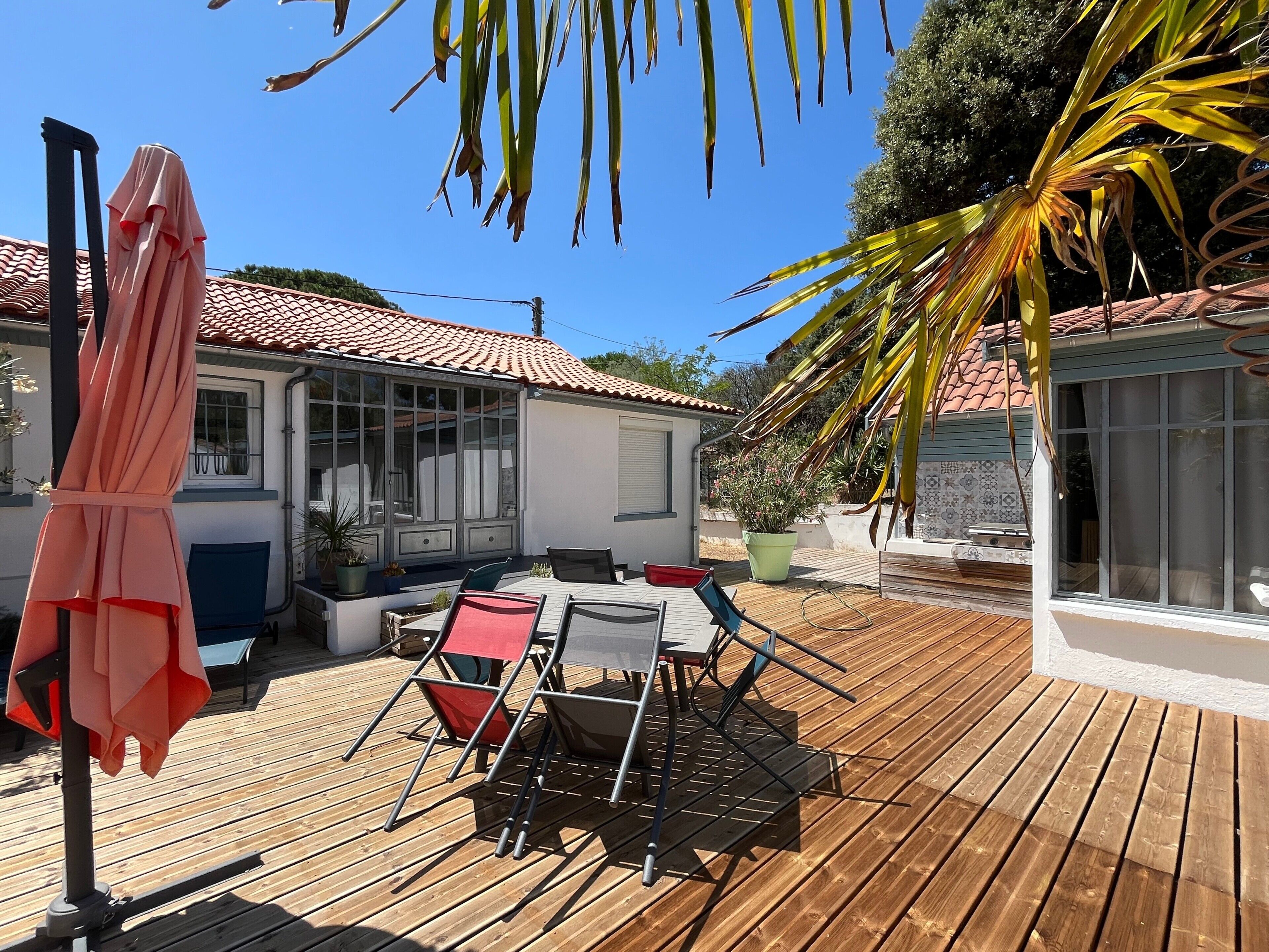 Une terrasse en bois avec des meubles d’extérieur, une table abritée et une plante en pot.
